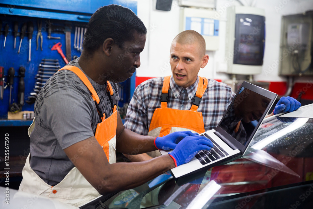 Two auto mechanics diagnosing car engine with laptop with special program at the car repair service center