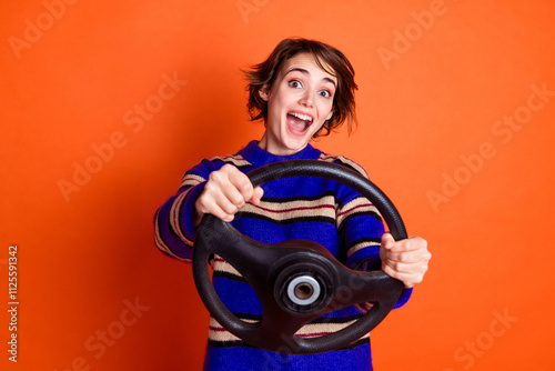 Photo portrait of young girl wearing striped blue sweater holding steering wheel driving first vehicle isolated on orange color background photo