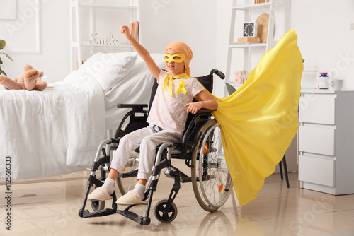 Little girl after chemotherapy dressed as superhero with yellow ribbon in wheelchair at hospital. Childhood cancer awareness concept photo