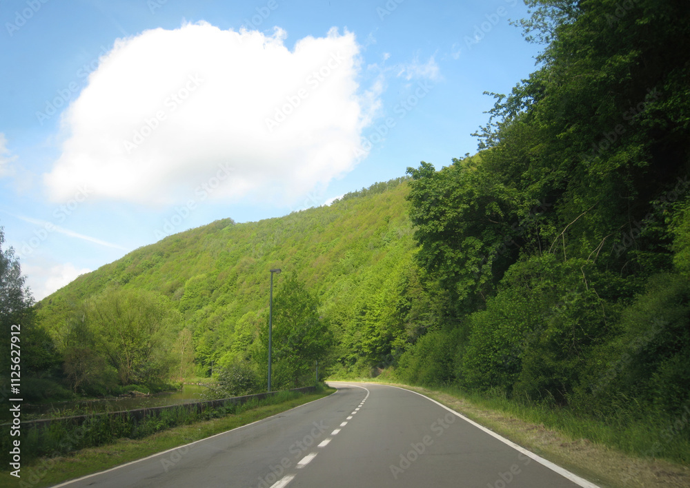Winding road through lush green hills on a sunny day Winding road through lush green hills on a sunny day