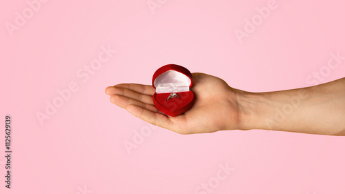 Fotografie Unrecognizable man holding box with engagement ring on orange background, closeup