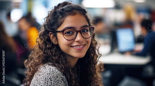 Portrait en gros plan d'une jeune femme souriante au travail, portant des lunettes, assise devant son équipe au bureau, arrière-plan flou de collègues. photo