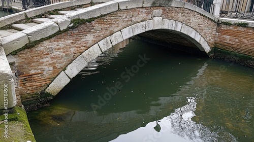 Old brick arch bridge over calm canal water.