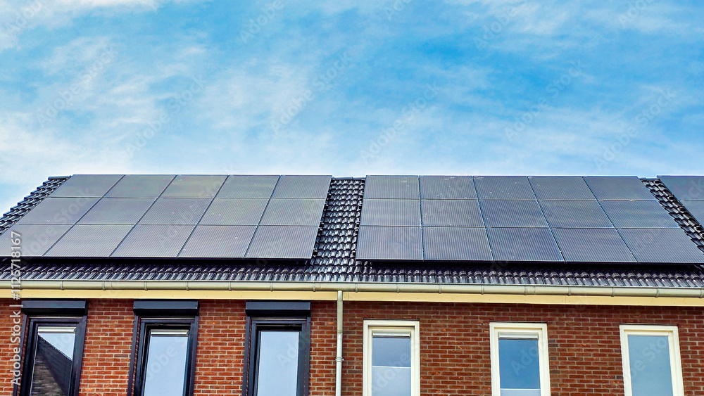 Fototapeta premium black solar panels on the roof against a sunny sky in the Netherlands, Close up of new building with black solar panels. Zonnepanelen, Zonne energie, Translation: Solar panel, Sun Energy