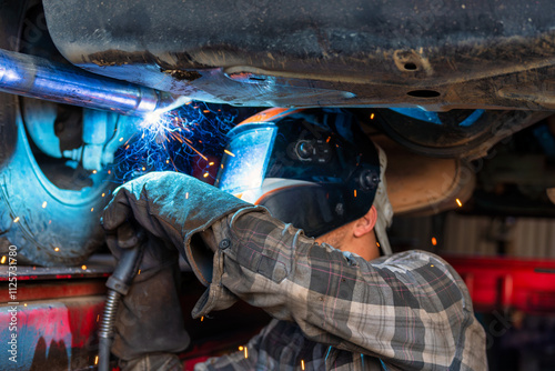A skilled Welding Mechanic is working diligently underneath a vehicle with sparks flying around