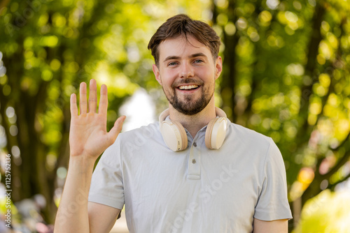 Hello, welcome. Athletic fit runner guy waving hi with palm greeting with hospitable friendly smile. Young Caucasian man jogger workout cardio training in park at morning. Active healthy sportsman.