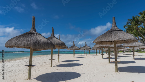 Rows of straw umbrellas on the sandy beach. Round shadows on the white sand. A calm turquoise ocean. Palm trees against a background of blue sky and clouds. Mauritius. photo