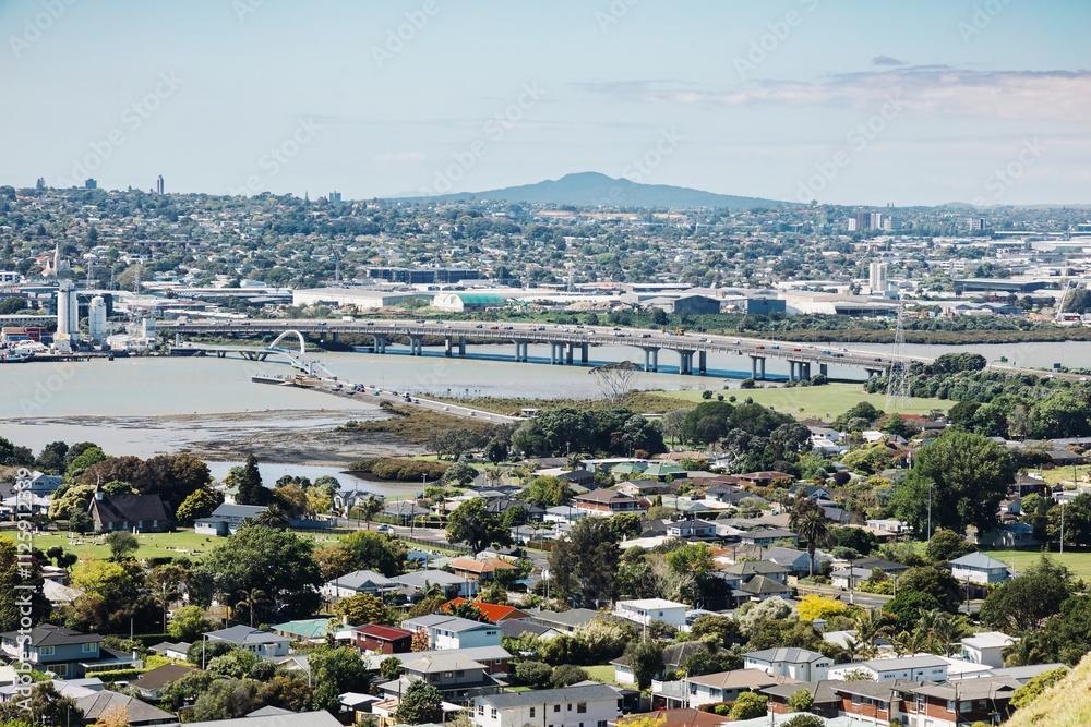 Naklejka premium MANGERE, AUCKLAND, AUCKLAND, NEW ZEALAND, High-angle view of a bustling city, showcasing residential areas in Onehunga, industrial zones, and a highway bridge spanning a river.