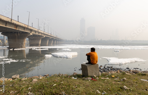 Isolated man looking at Toxic Foam in Contaminated River with Bridge Near Foggy City at morning photo