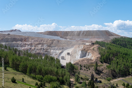 Expansive open pit gold mining operation in Colorado with heavy machinery working on a sunny day amidst lush greenery and distant mountains