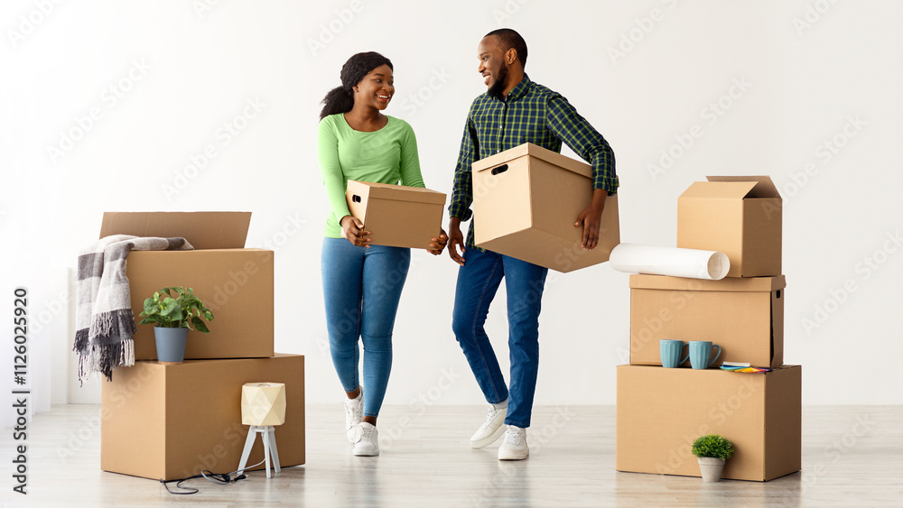 Home Relocation Concept. Portrait Of Joyful African American Spouses Walking With Cardboard Boxes After Moving To New Flat, Happy Black Couple Carrying Belongings And Smiling To Each Other
