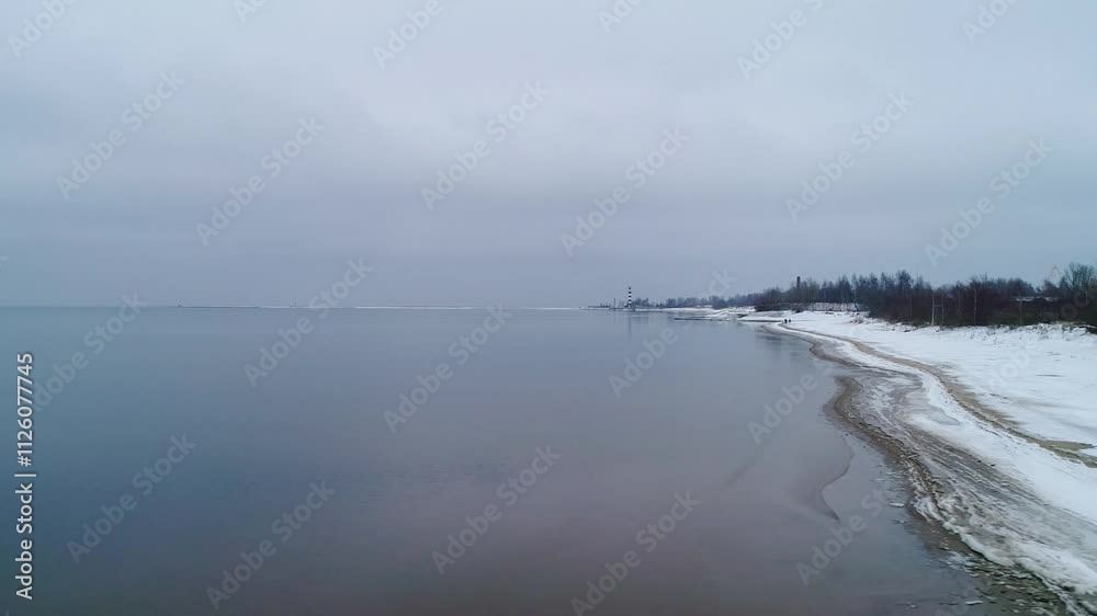 Drone moves leftward over a snowy coastline - calm sea meets the winter horizon