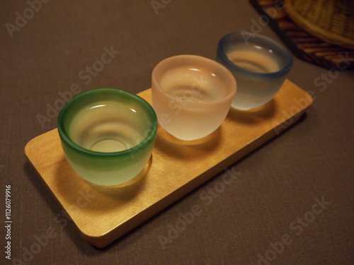 Welcome drinks served on the table for tasting, Three filled with Japanese matte glass sake cups of different colors on wooden tray