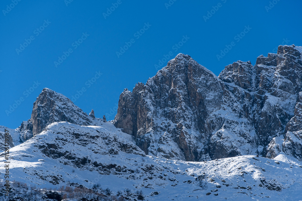 Obraz premium Snowy peaks and glaciers cover giant rocks. Pine and spruce forests grow at foot of mountains. which Majestic mountains against blue sky. Sunny day. Autumn 2024. Karachay-Cherkessia. Dombay.