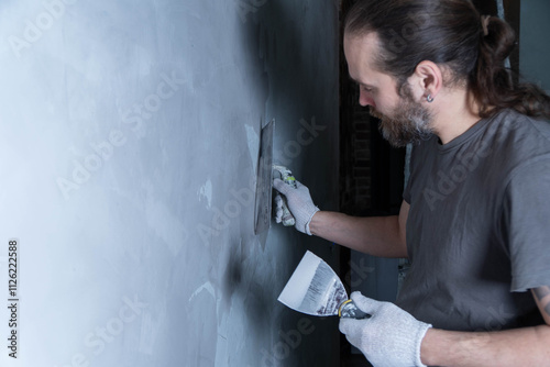 Skilled worker is using microcement to fix a damaged wall in a residential space.