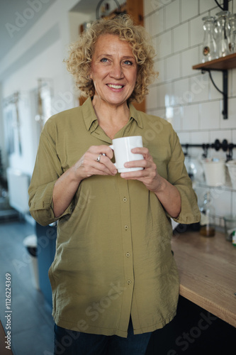 Happy middle-aged woman enjoying fresh aromatic coffee in the ki photo