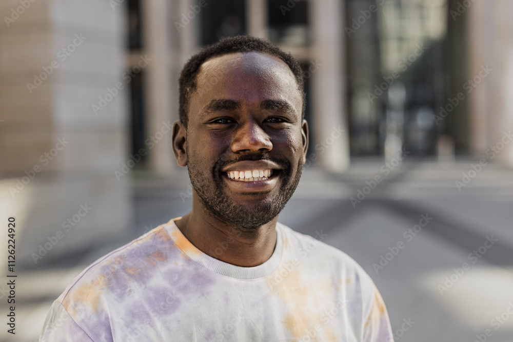 Cheerful African American young man standing near urban building Cheerful African American young man standing near urban building