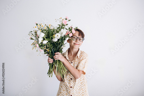 Boy holding large bouquet of flowers against white wall photo