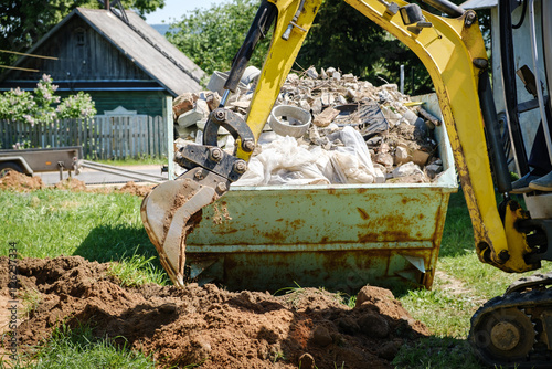 Mini excavator digs a narrow trench in soil for laying communications close-up. Mini bucket of crawler machine. Earthworks with heavy special equipment. Digging machinery works at construction site photo