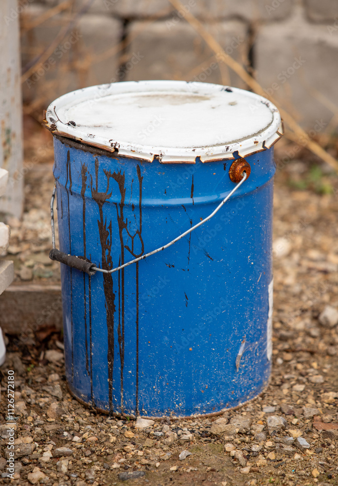 A blue bucket with a white lid sits on the ground A blue bucket with a white lid sits on the ground