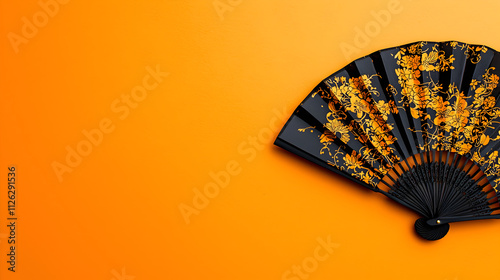 Black hand fan with gold floral pattern on orange background. photo