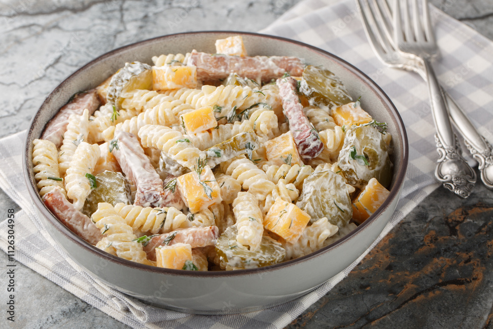 Creamy pickles pasta salad with yellow cheese, herbs and bacon close-up in bowl on table. Horizontal Creamy pickles pasta salad with yellow cheese, herbs and bacon close-up in bowl on table. Horizontal