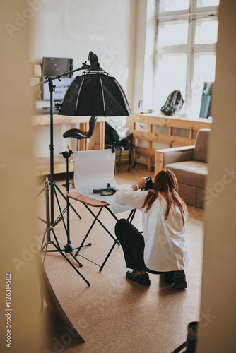 Female photographer taking photo of objects on background in photo studio with professional equipment