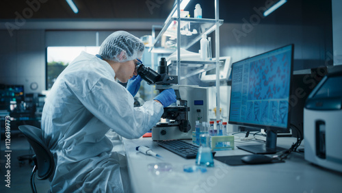 Medical Research Scientist Working in a Sterile Laboratory, Wearing Protective Uniform, Hat and Silicone Gloves. Researcher Looking at a Specimen Under a Microscope