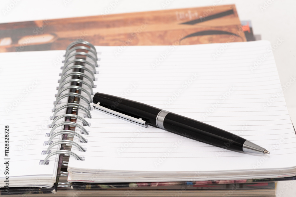 A black pen is on a white page of a spiral bound notebook A black pen is on a white page of a spiral bound notebook