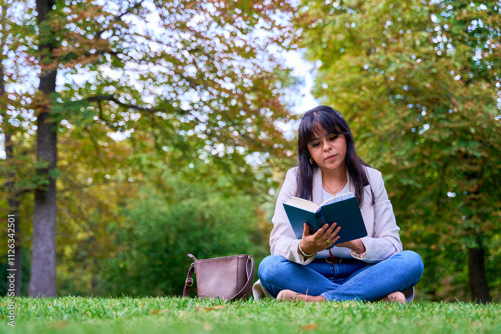 Latina woman reading a book while sitting on the grass in a park Latina woman reading a book while sitting on the grass in a park