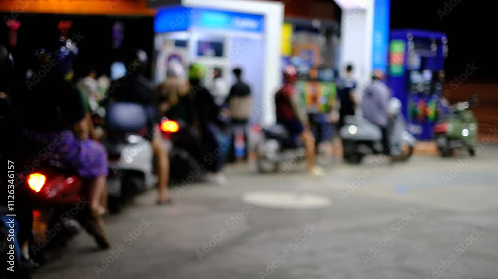 A group of people are standing around a gas station. There are several motorcycles parked in the area A group of people are standing around a gas station. There are several motorcycles parked in the area