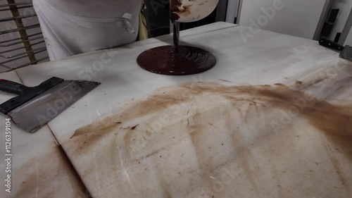 A caucasian pastry chef working with hot chocolate on a white marble table in his workshop for his sweets. photo