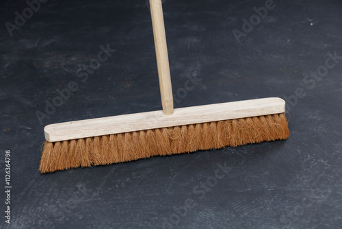 Close-up of a broom with natural brown bristles on a dark gray surface.  Cleaning tool.