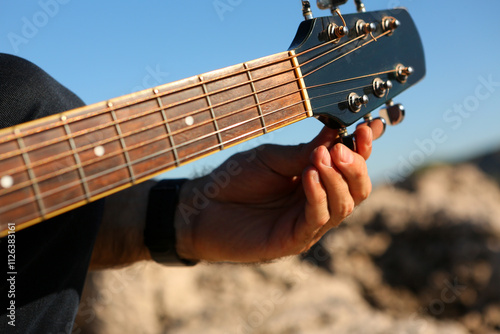 Close-up of a man tuning an acoustic guitar outdoors
