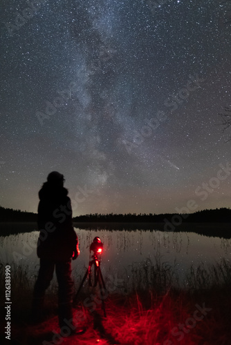 A person takes a photo of the night sky showing the Milky Way and a comet