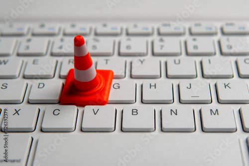 A miniature traffic cone placed on a computer keyboard. Website maintenance, technical difficulties, website under construction concept.