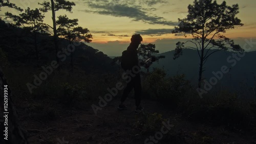 A young man holds a microphone to record his surroundings against the backdrop of a mountain sunset photo