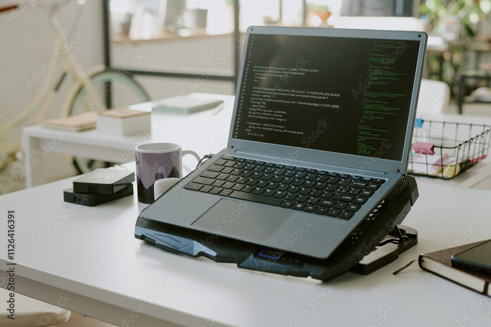 Medium close up of laptop with codes on cooling pad in empty office of IT company Medium close up of laptop with codes on cooling pad in empty office of IT company
