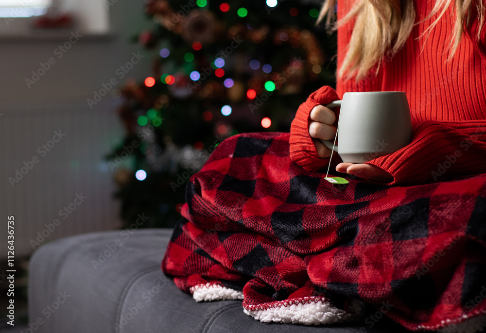 Close up of a woman holding a mug with hot drink and sitting on a sofa with a red blanket Close up of a woman holding a mug with hot drink and sitting on a sofa with a red blanket