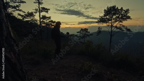 A young man holds a microphone to record his surroundings against the backdrop of a mountain sunset photo