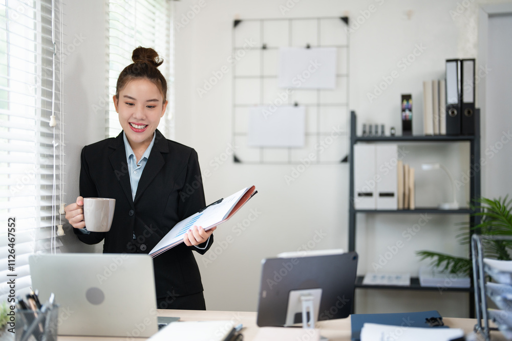 Smiling woman enjoying a coffee break at home office desk with laptop and documents, working in a bright and comfortable environment.