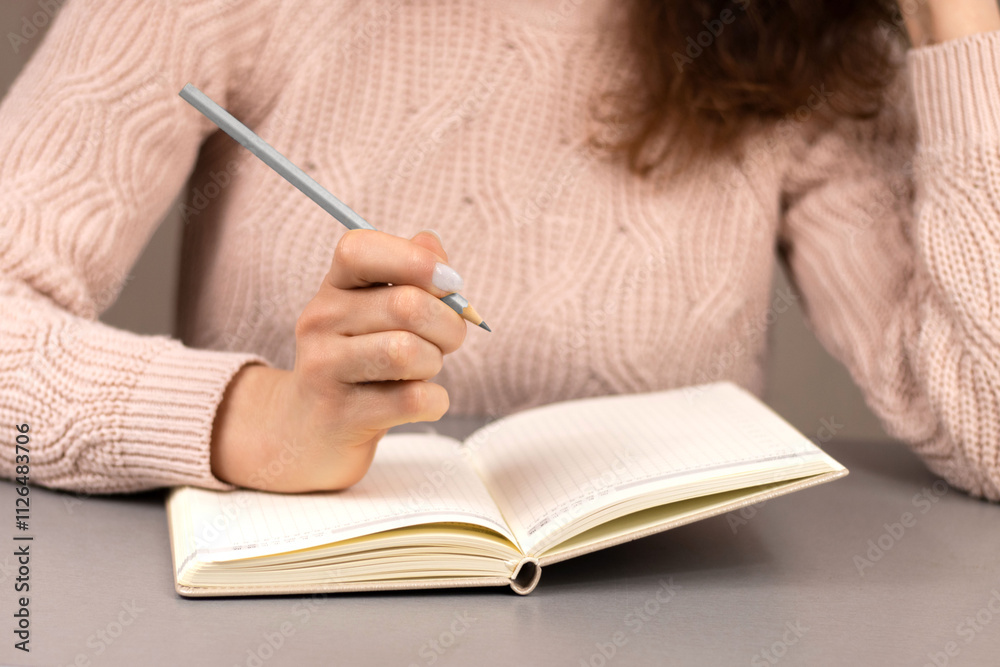 Female hand holding a gray pencil to make an entry in a notebook
Hand of a person close-up at a table to write down a note or planning or studying. Female hand holding a gray pencil to make an entry in a notebook
Hand of a person close-up at a table to write down a note or planning or studying.