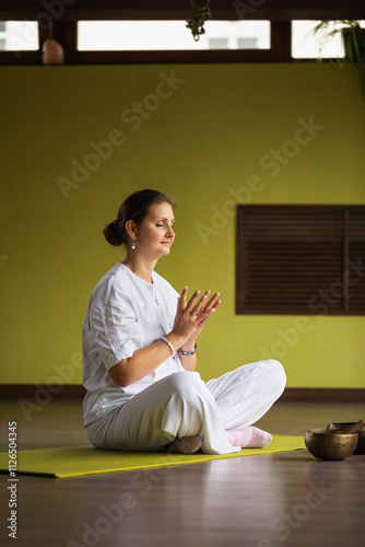 A woman makes the Lotus mudra while sitting in a comfortable position on a mat in a yoga studio, leads a healthy lifestyle, practices Kundalini Yoga meditating with her eyes closed