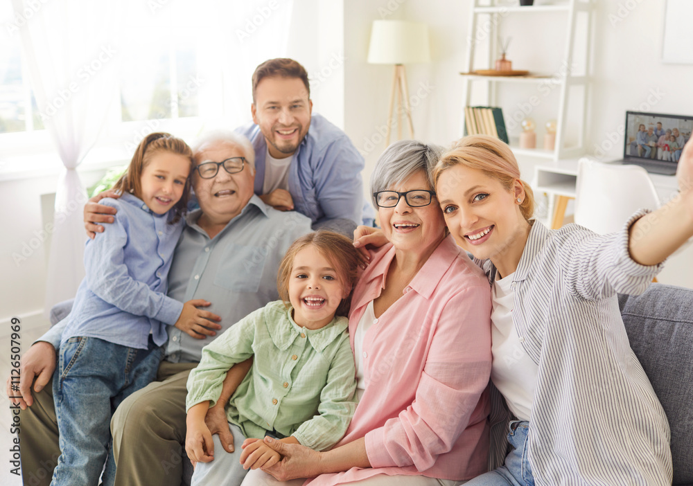 Portrait of happy cheerful big family of young parents, senior grandparents and two smiling children boy and girl looking at camera making selfie together sitting on sofa in living room at home. Portrait of happy cheerful big family of young parents, senior grandparents and two smiling children boy and girl looking at camera making selfie together sitting on sofa in living room at home.