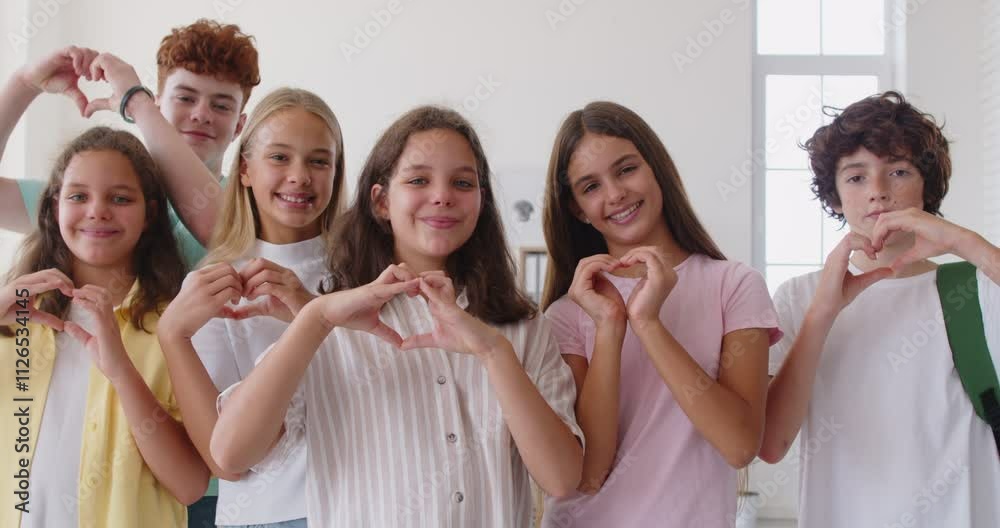 Unity and friendship. Group of energetic schoolchildren enthusiastically showing the camera hearts with their own hands. Preteen boys and girls in school classroom make heart shape with their hands. Unity and friendship. Group of energetic schoolchildren enthusiastically showing the camera hearts with their own hands. Preteen boys and girls in school classroom make heart shape with their hands.