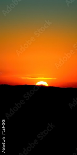 Vibrant orange and yellow sunset over a silhouetted landscape, setting sun