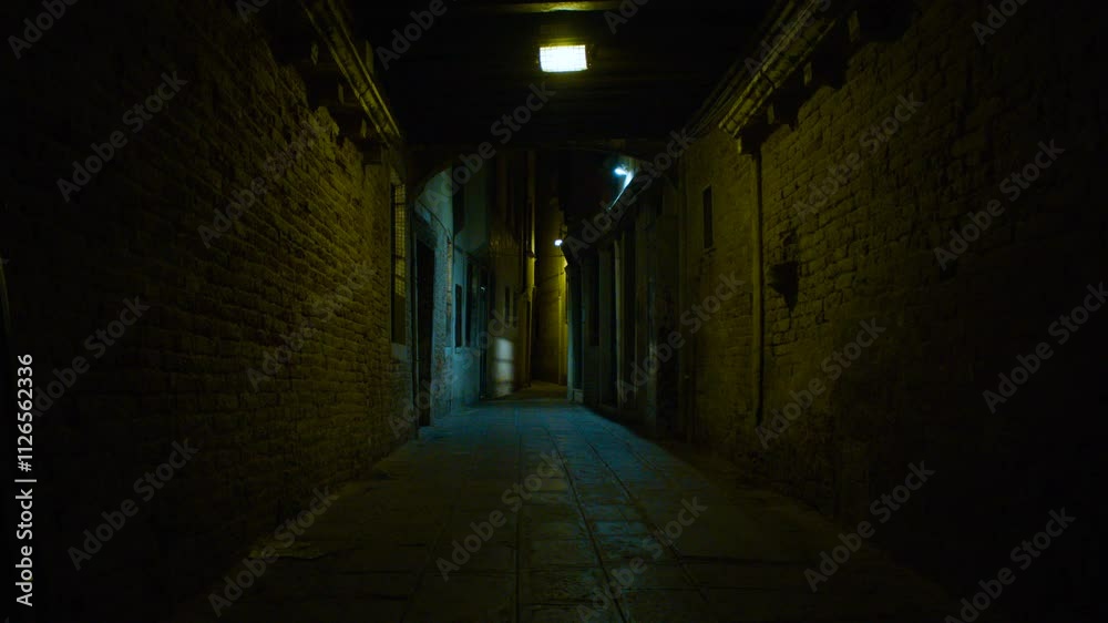 Tilt shot of a long narrow alley illuminated with dim light. Beams of blue and yellow light illuminate a narrow urban passageway. Tilt shot of a long narrow alley illuminated with dim light. Beams of blue and yellow light illuminate a narrow urban passageway.