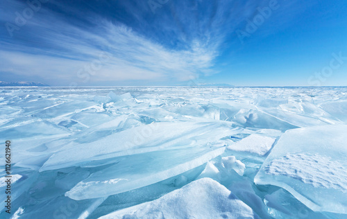 Winter natural background with fragments of blue snowy ice and heaps of pieces of ice floes on frozen Baikal Lake on sunny frosty day. Beautiful blue sky with layered clouds. Scenic winter landscape