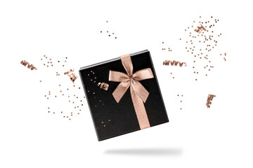 Black gift box with copper golden ribbon and confetti flying isolated on white background. Black friday or celebration concept. Ribbon and confetti in trendy color  Mocha Mousse.