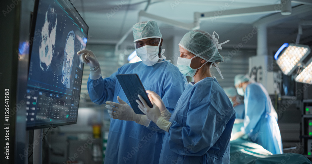 Black Male and Caucasian Female Surgeons Analyze Brain Scans on a Digital Monitor, Planning Surgical Strategy in a High-tech Operating Room. Colleagues Working Together, Preparing for Surgery